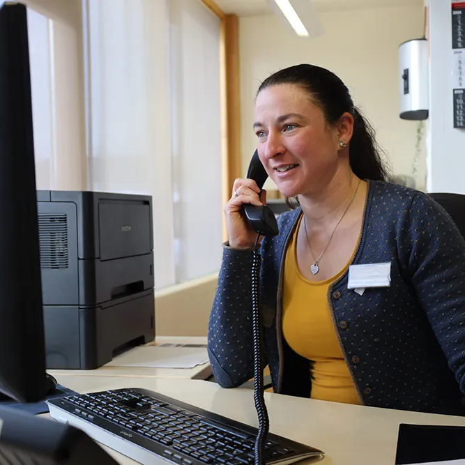 In einem hellen Büroraum spricht eine Mitarbeiterin der Ferienregion am Telefon, ihre Mimik zeigt Freundlichkeit und Engagement.