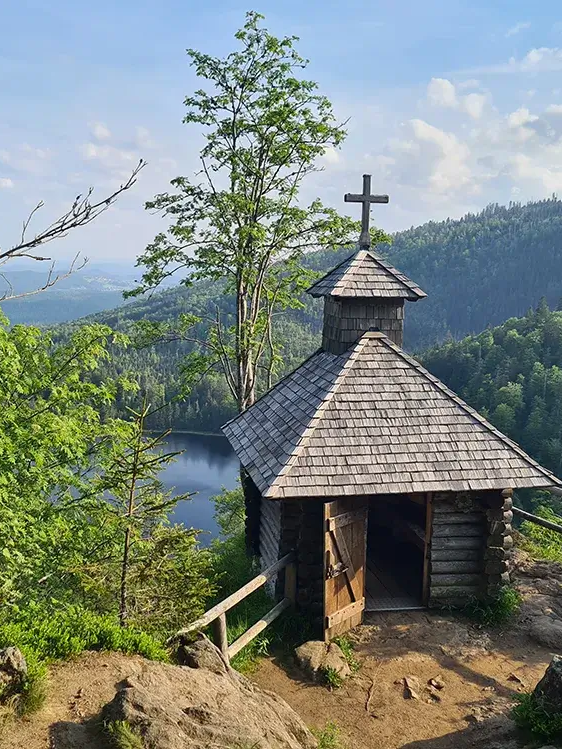 Die hölzerne Rachelkapelle thront oberhalb des Eiszeitsees und strahlt Ruhe aus, während sie von Bäumen eingebettet ist und den Blick auf den Rachelsee freigibt.