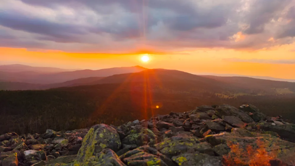 Warme Farben bestimmen den unvergesslichen Sonnenuntergang über dem Granitgipfel mit Blick vom Lusen auf die entfernte Bergwelt davor.