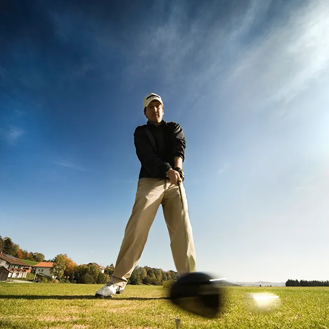 Golfer in Aktion: Perfekter Schwung auf gepflegtem Golfrasen Ein Golfer in sportlicher Kleidung bereitet sich auf einen Abschlag auf dem sonnigen Golfplatz vor.