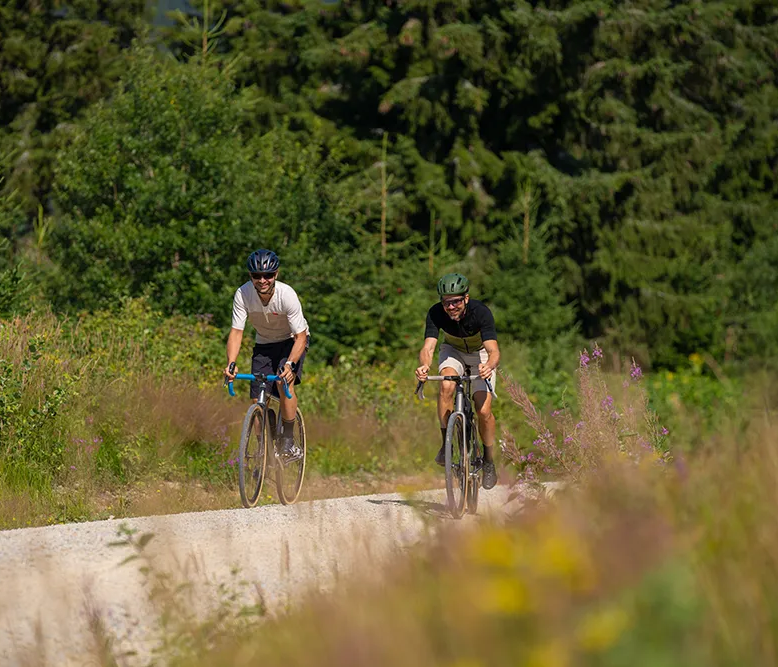 Zwei Radfahrer sind auf einem sonnigen Schotterweg in der Ferienregion Nationalpark Bayerischer Wald unterwegs und erfreuen sich an der üppigen und abwechslungsreichen Natur