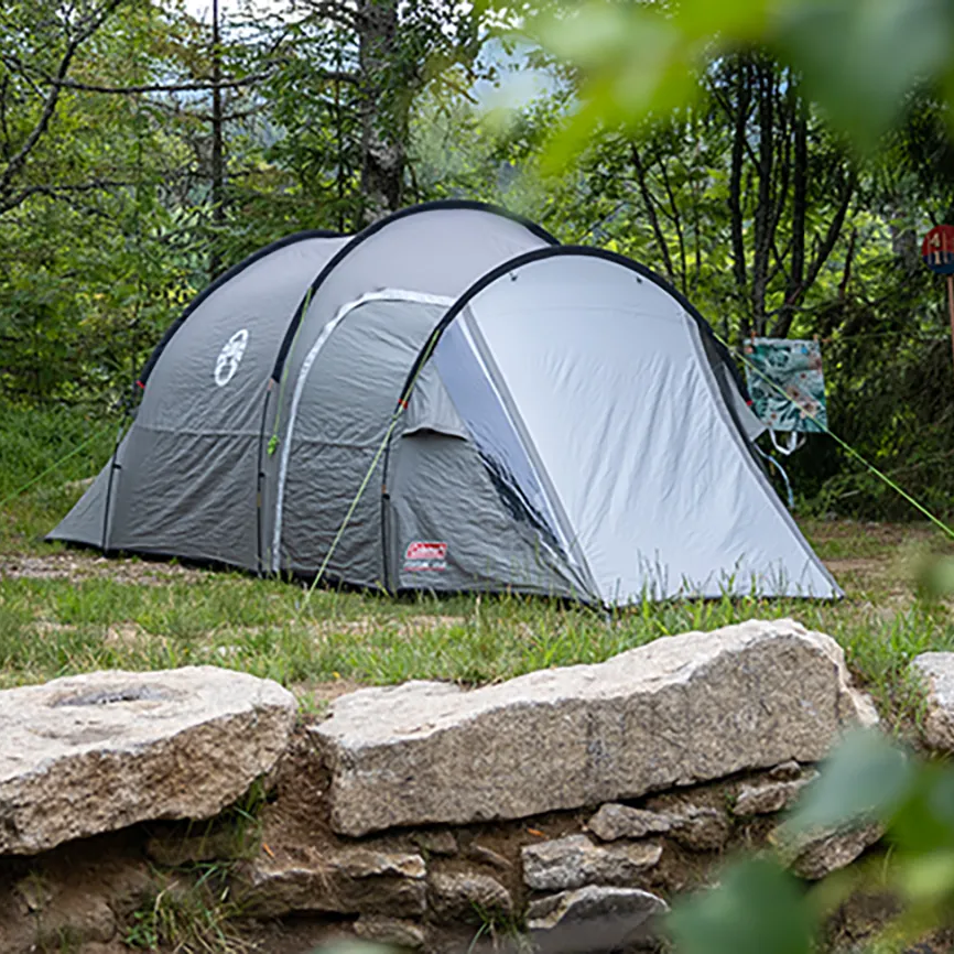 Ein graues Zelt steht auf einem angelegten Platz, umgeben von Bäumen und einer ruhigen, naturnahen Umgebung.