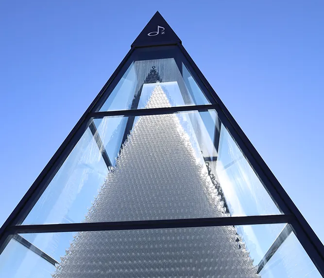Ein kunstvolles Bauwerk aus unzähligen Kristallgläsern, das in Form einer Pyramide gestaltet ist, steht unter einem strahlend blauen Himmel in der Glasstadt Zwiesel.