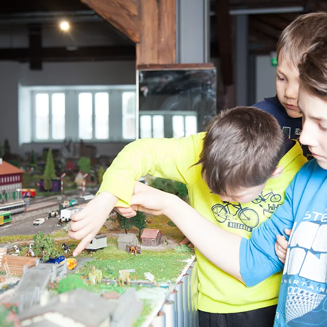 Die Jungen sind fasziniert von der Modelleisenbahn im Naturparkmuseum in Bayerisch Eisenstein, während sie auf die kleinen Figuren und Züge in der Anlage zeigen.