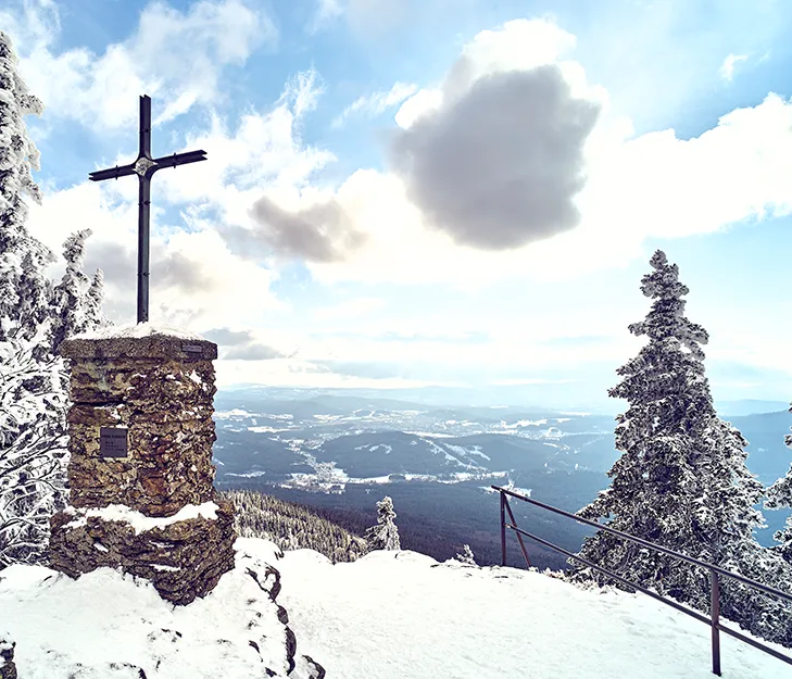 Das Kreuz auf dem Berggipfel steht majestätisch im Schnee, während die Wolken über der winterlichen Landschaft ziehen.