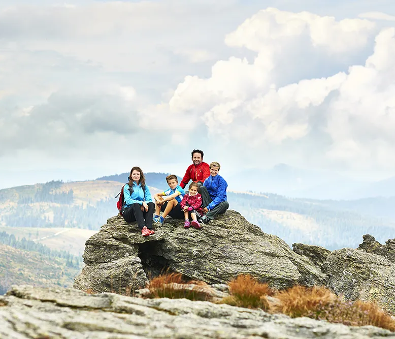 Die Gruppe von fünf Personen, darunter Kinder, verbringt eine kurze Auszeit auf einem Felsen mit Blick auf die weite Bayerwaldlandschaft.