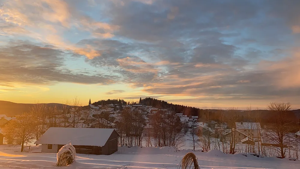 Ein Wintermorgen wie aus dem Bilderbuch, mit schneebedeckten Hügeln und einem warmen Sonnenaufgang, der den Himmel in sanften Farben erleuchtet.