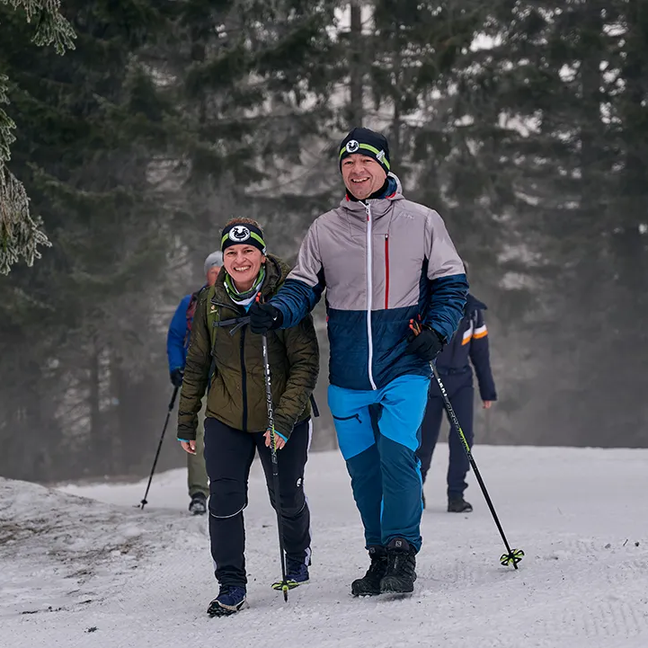 Ein fröhliches Paar wandert auf einem verschneiten Weg durch die Wälder der Ferienregion Nationalpark Bayerischer Wald