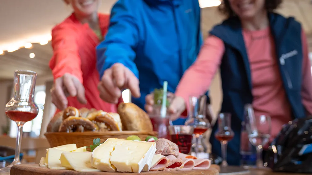 Eine gesellige Runde genießt regionale Spezialitäten, während sie sich um eine Holzplatte mit Snacks versammelt.