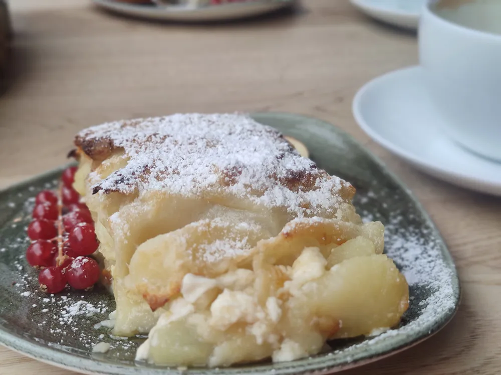 Ein Stück Apfelstrudel typisch aus dem Bayerwoid mit Puderzucker und roten Johannisbeeren auf einem Keramikteller serviert, auf einem Kaffetisch.