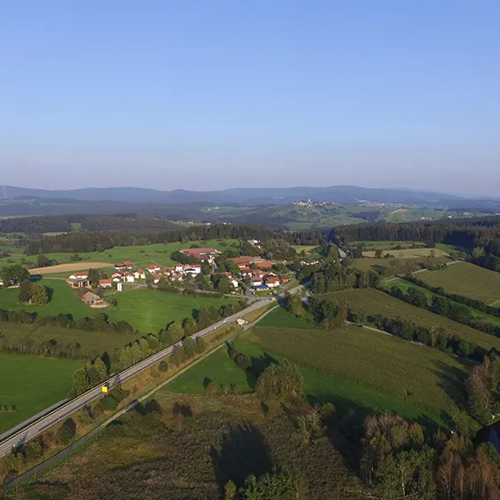Luftaufnahme des Ortsteils Haslach mit dem Hohenauer Badesee Eine weite Aussicht auf das Örtchen Haslach, umgeben von weiten Wiesenfeldern und Waldflecken, mit dem ruhig gelegenen Hohenauer Naturbadesee, der die natürliche Schönheit noch ergänzt.