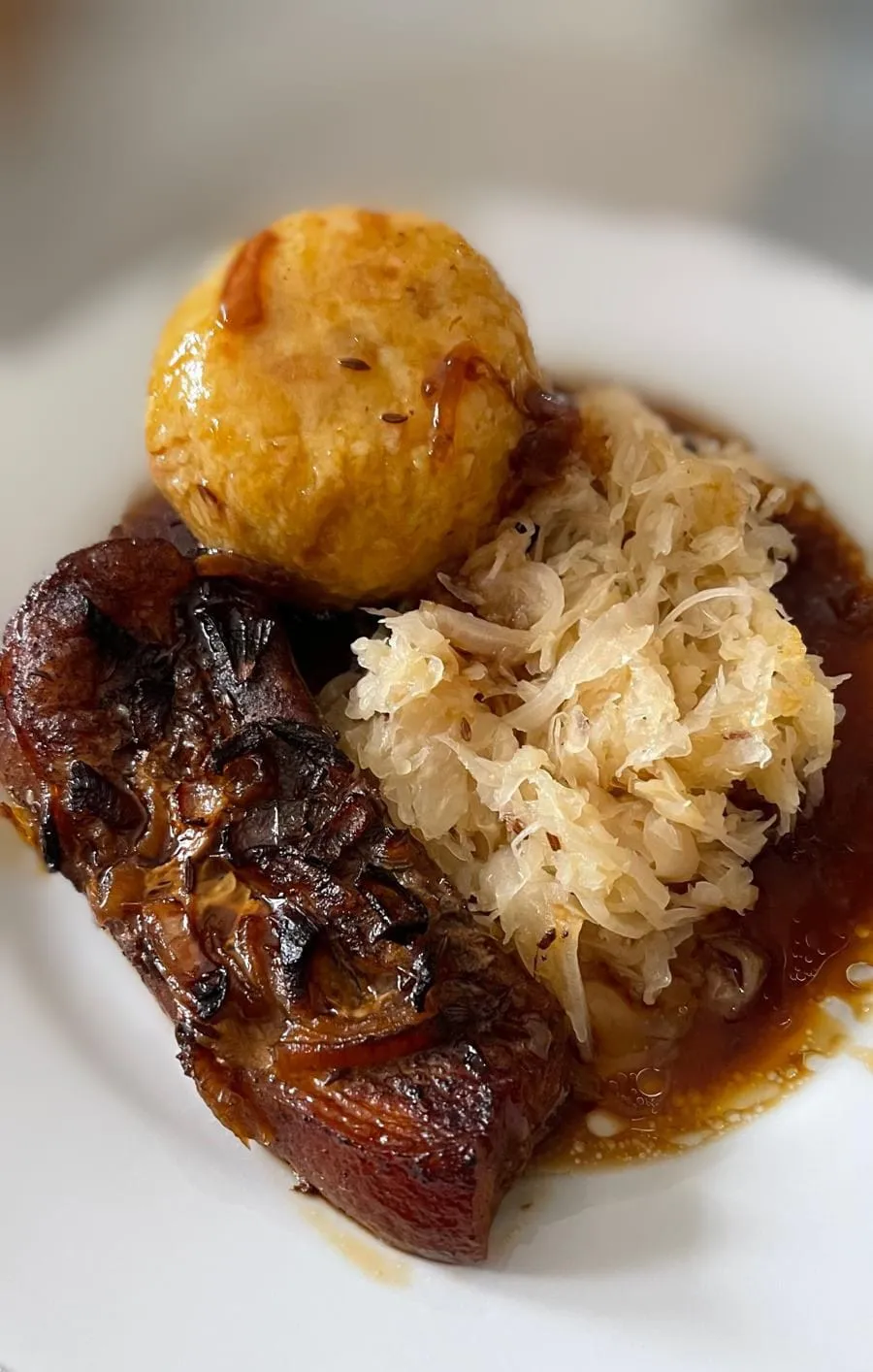 Ein herzhafter Schweinebraten mit saftigem Fleisch und Soße, einem goldenen Knödel und einer Portion Sauerkraut auf einem weißen Teller.