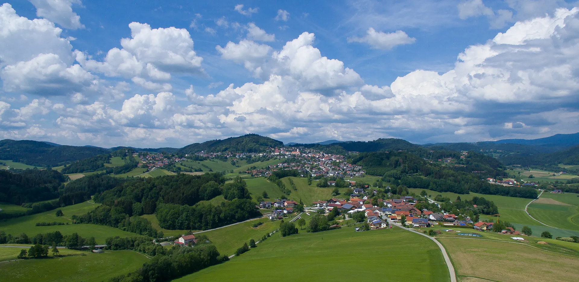 Drohnenblick auf das sogenannte Meran des Bayerischen Waldes, umrahmt von hellgrünen Wiesen und bewaldeten Waldwogen