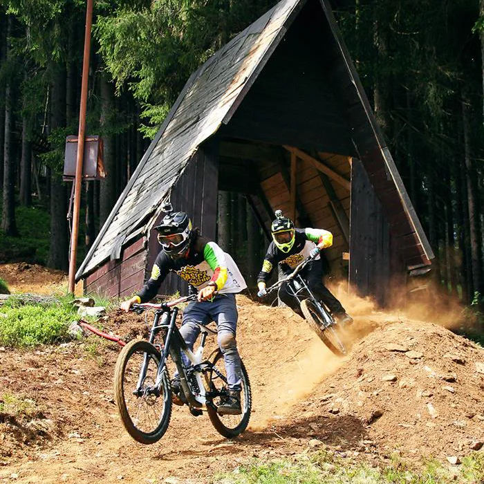 Zwei Mountainbiker fahren sportlich einen Hang hinunter, das teilweise Staub aufwirbelt
