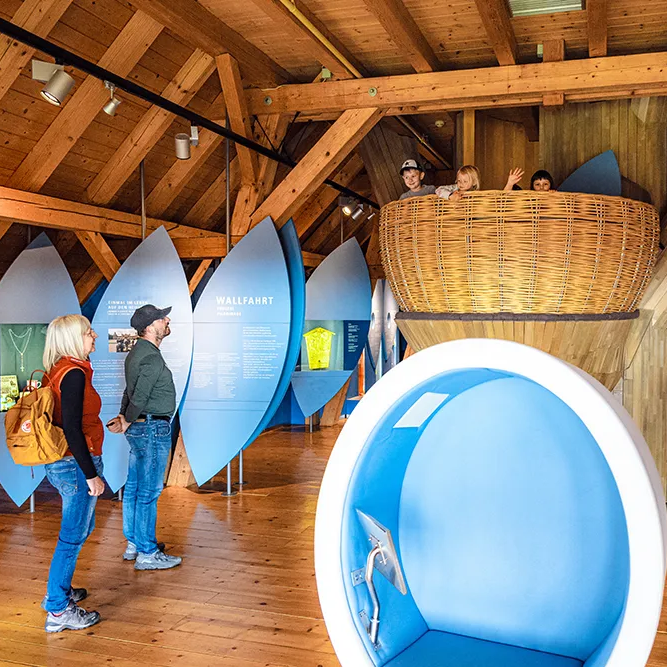 Zwei Besucher betrachten das Nest des begehbaren Baums im Waldgeschichtlichen Museum, während Kinder erfreut herausschauen. 
