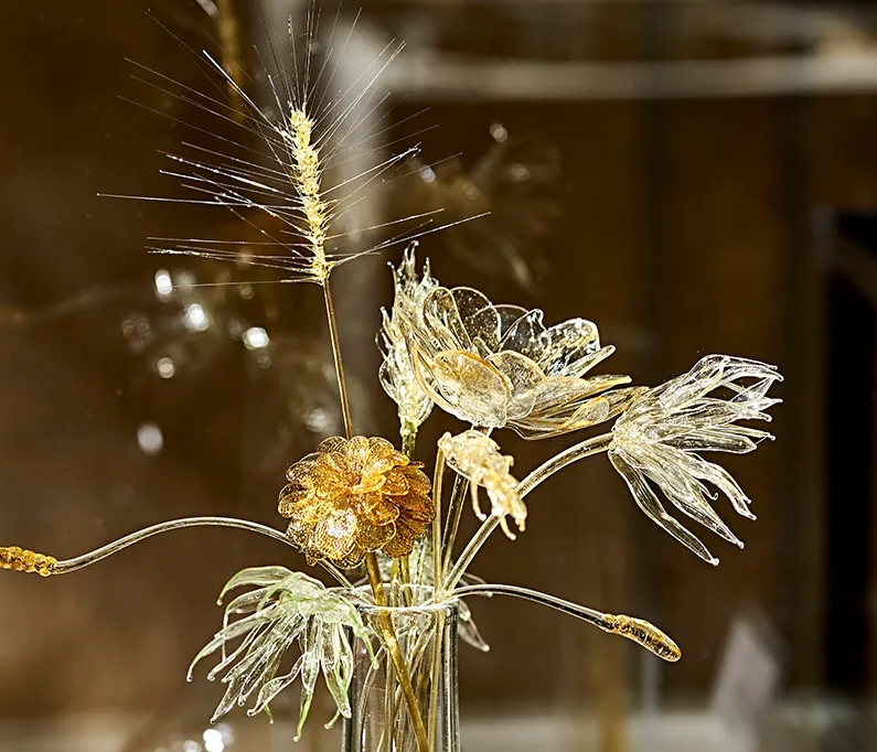 Die Komposition zeigt filigrane, gläserne Pflanzen mit goldenen Akzenten, die im Glasmuseum Frauenau ausgestellt waren.