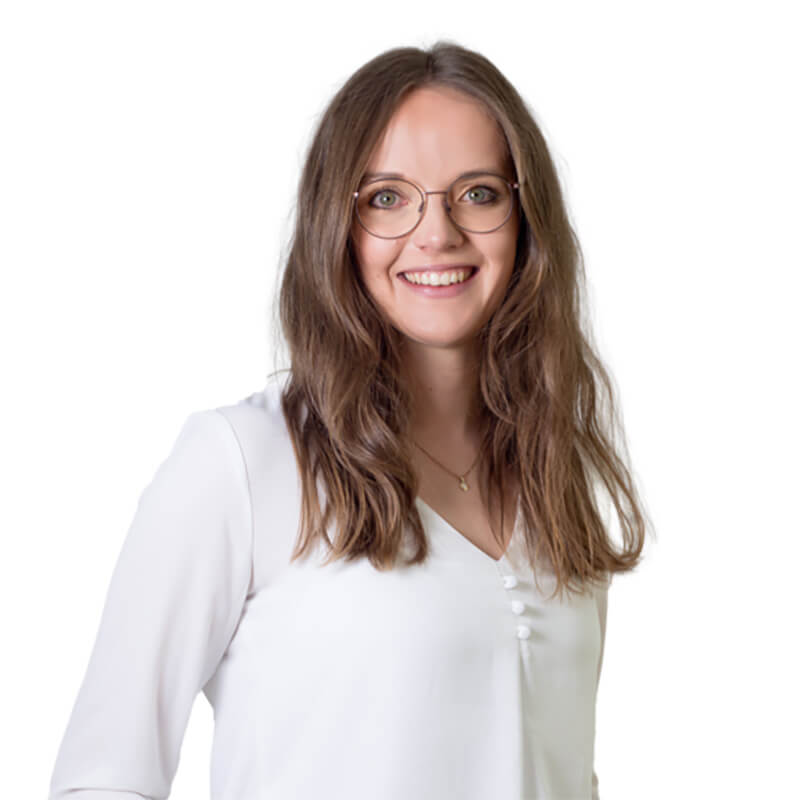 Das Bild zeigt die lächelnde Mitarbeiterin, Andrea Kralik, mit langen, lockigen Haaren, in weißer Bluse.